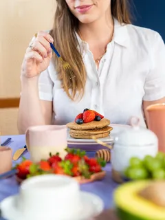 Kvinna vid bord med frukost och frukt på tallrik